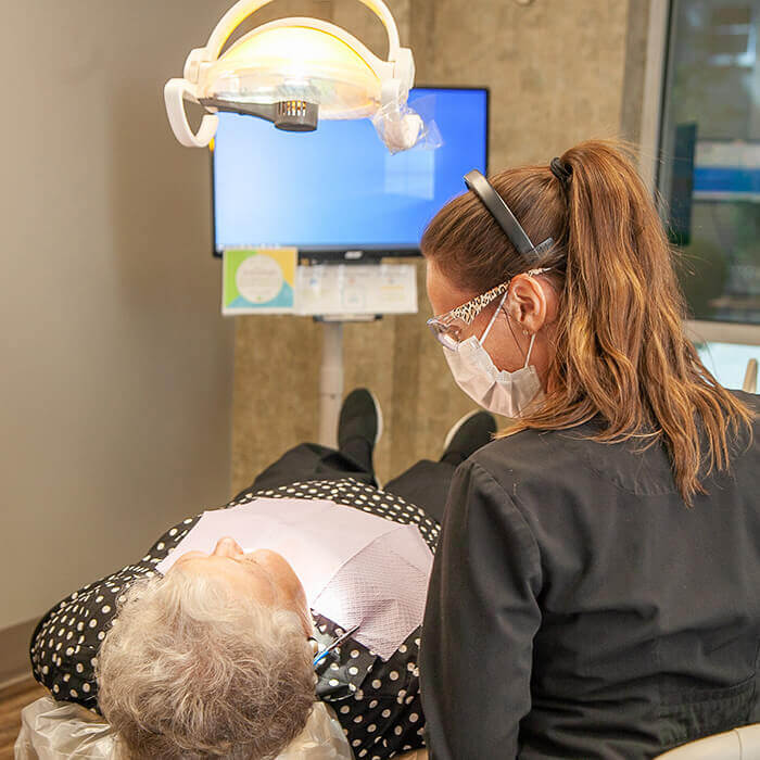 Schedule a regular dental check ups with us An old female patient lying in a dental chair during a dental procedure and a team member looking towards the patient