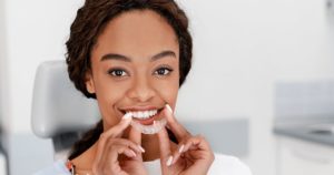 Young woman holding a clear aligners to her mouth.