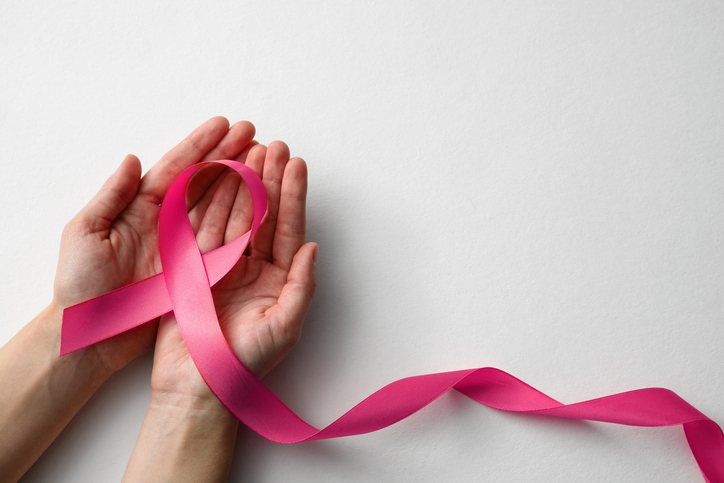 Person holding a pink ribbon in their hands to celebrate breast cancer awareness